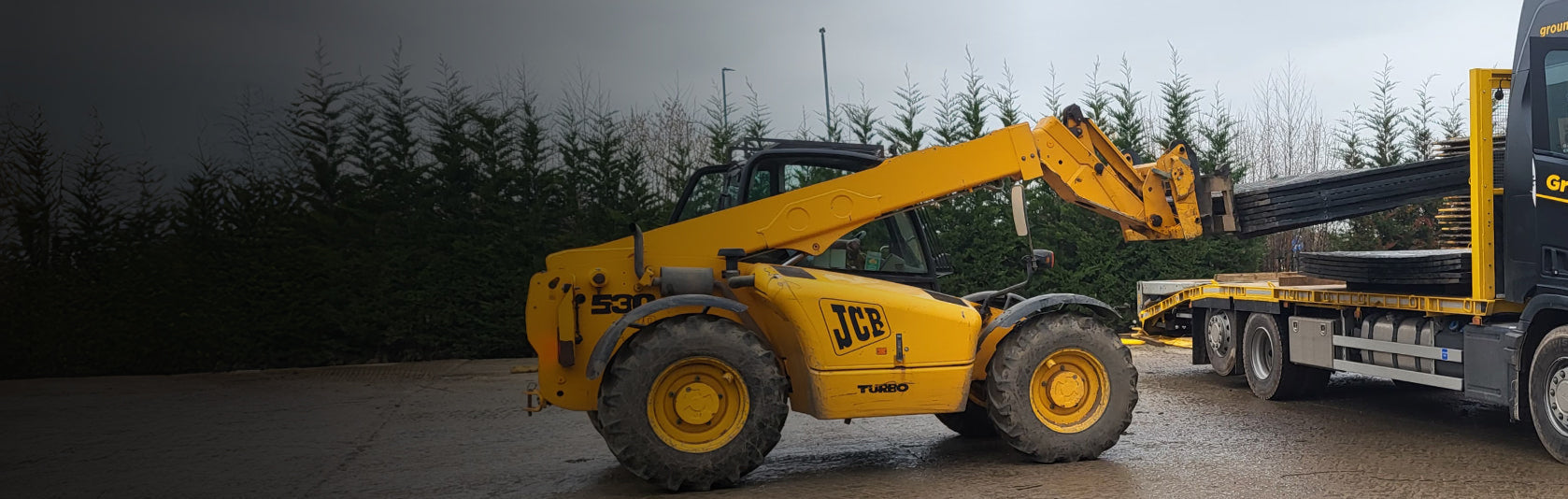 Scania truck being loaded by a yellow telescopic handler with ground protection mats.