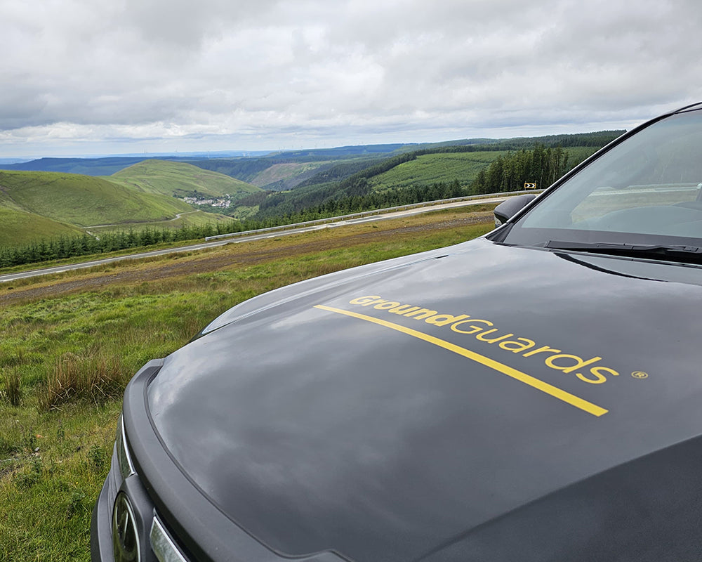 Car hood with 'groundGuards' logo against a scenic background of hills and sky.